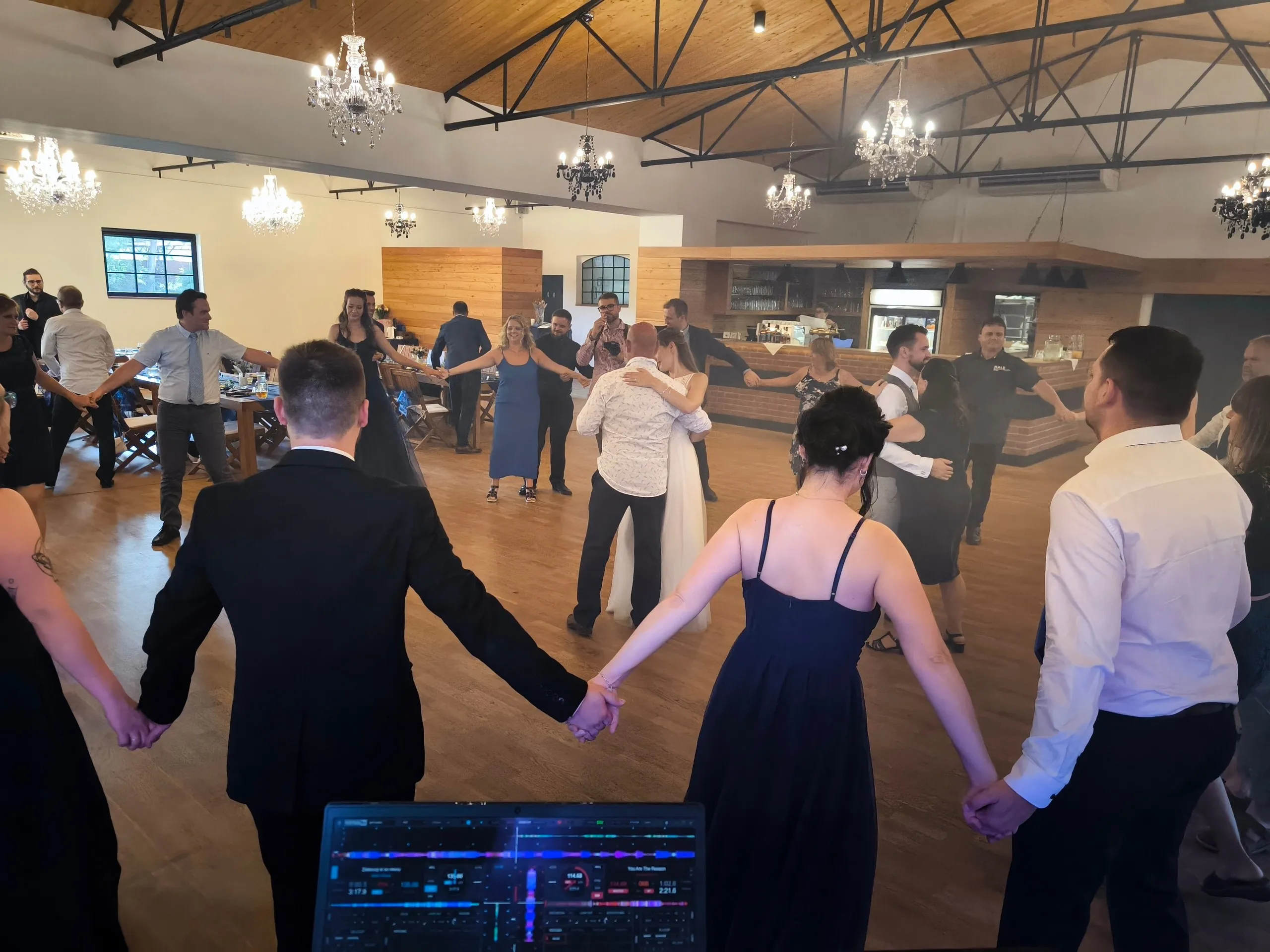 Kolo tančících svatebních hostů pohledem od DJ pultu